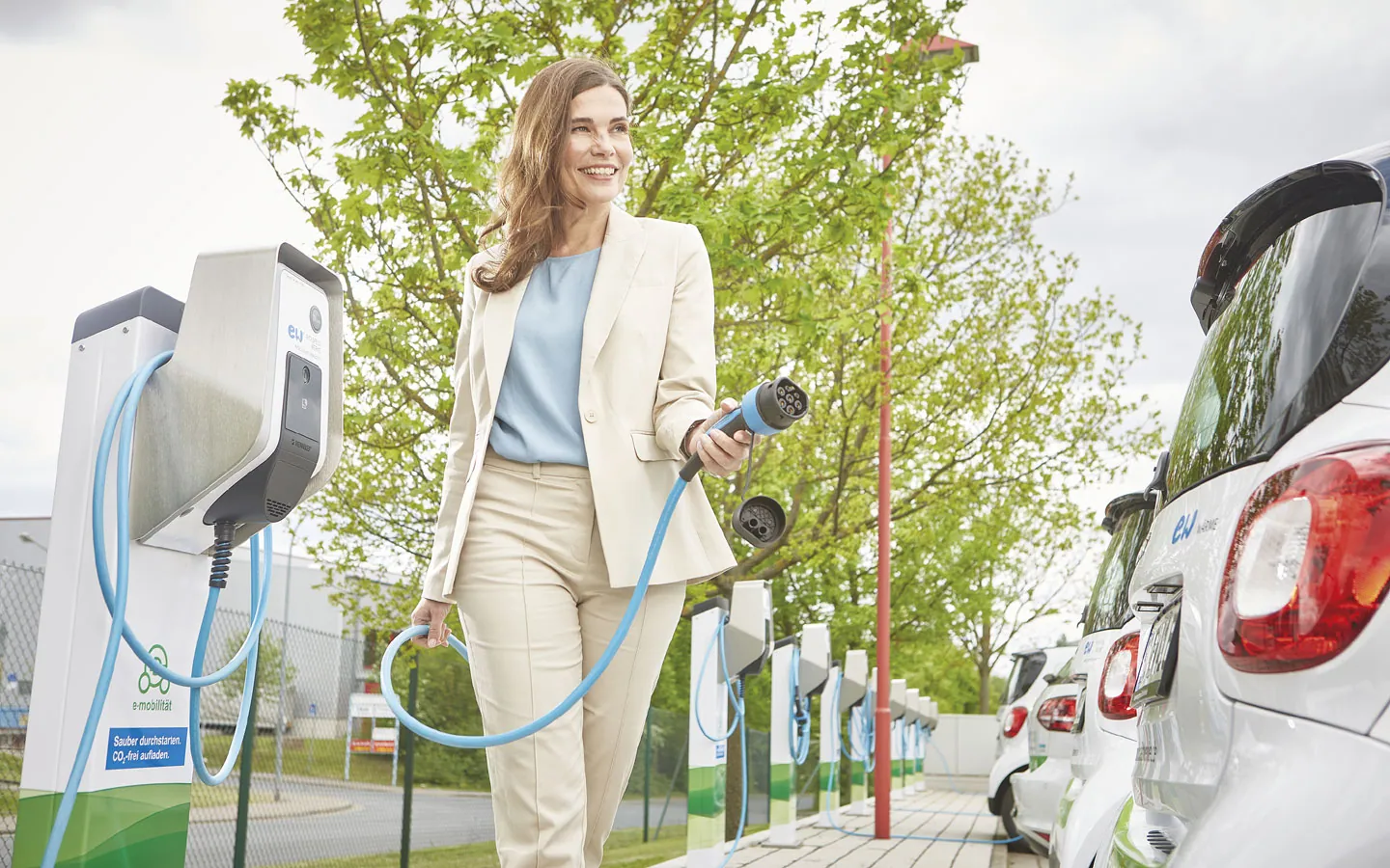 E-Mobilität - Kundin vor Ladestation mit Stecker in der Hand · Elektro-Stock